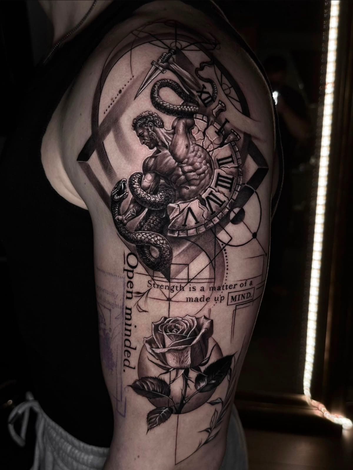 Atlas mit Uhr, Schlange und feiner Schrift auf dem Oberarm